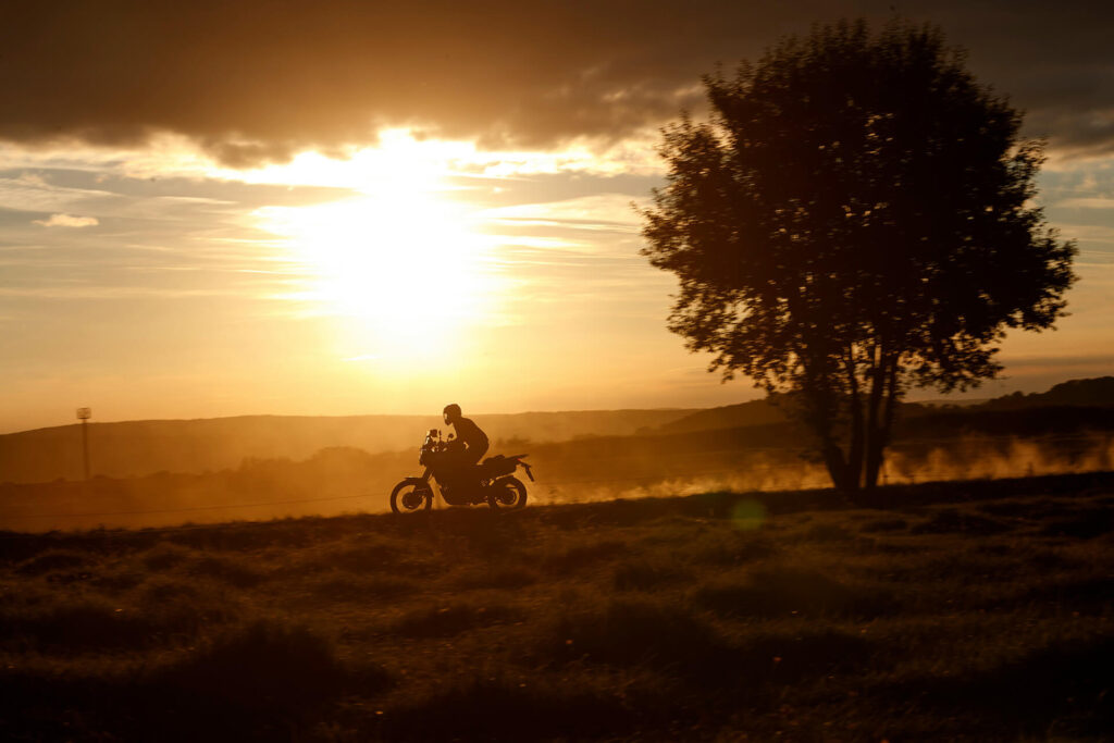 Motocyklista jadący pod górę podczas wycieczki enduro na tle zachodzącego słońca